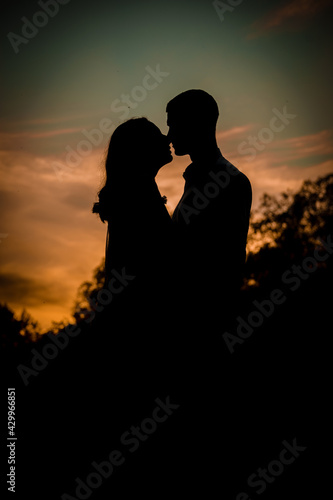 A dark silhouette of a woman and a man in love against the background of a sunset sky with clouds.