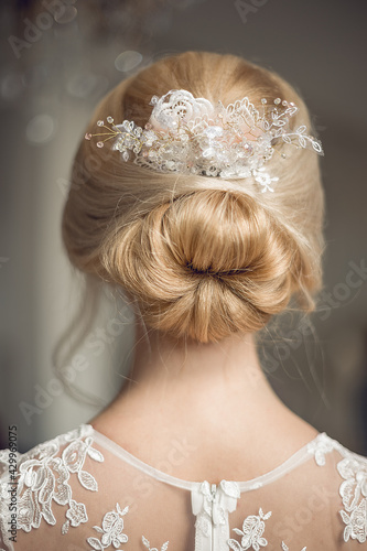 Young beautiful girl bride blonde from the back in a lacy white wedding dress. Blonde long hair in a bun with a beautiful lace decoration.