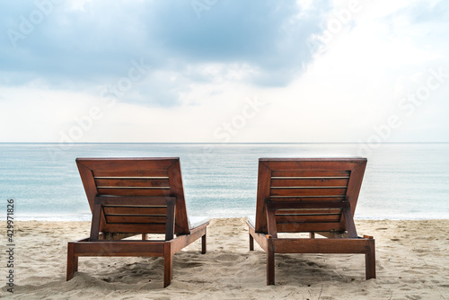 Back view of two wooden sunbeds together on the beautiful beach in the morning, the background of a wide-open view of sea and horizon, blank space for copy. © dul_ny