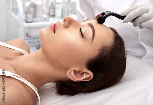 Beautician doing skin treatment using a microneedle dermaroller. Woman having procedure skincare with micro derma facial roller photo