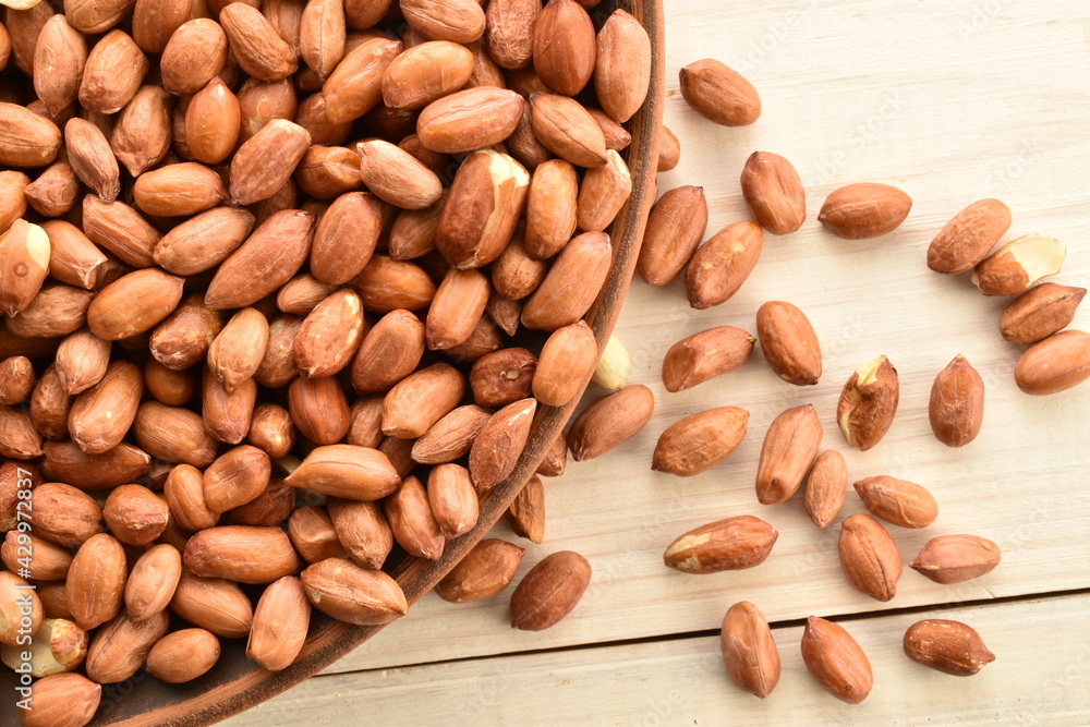 Many grains of organic peeled peanuts in a clay plate, on a wooden table, close-up, top view. Many grains of organic peeled peanuts in a clay plate, on a wooden table, close-up, top view.