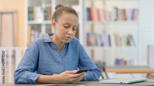 Bored African Woman Scrolling on Smartphone in Library
