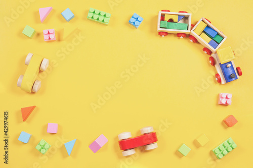 Baby kids toys background. Wooden train, car, colorful bricks and blocks on light yellow background. Top view