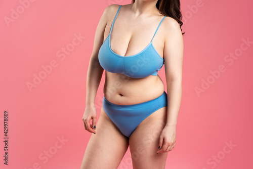 Fat woman with very large breasts in blue underwear on pink background, body care concept