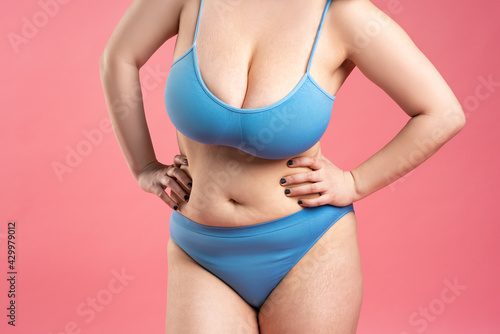 Fat woman with very large breasts in blue underwear on pink background, body care concept
