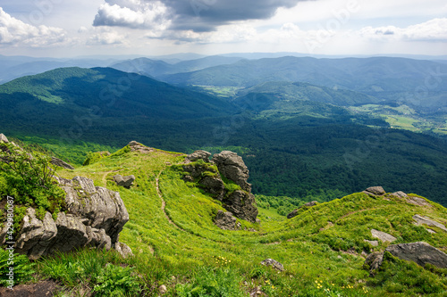 view from pikui mountain. huge stones on the grassy slopes. summer landscape of carpathian mountains. borzhava ridge in the distancee beneath a sky with clouds