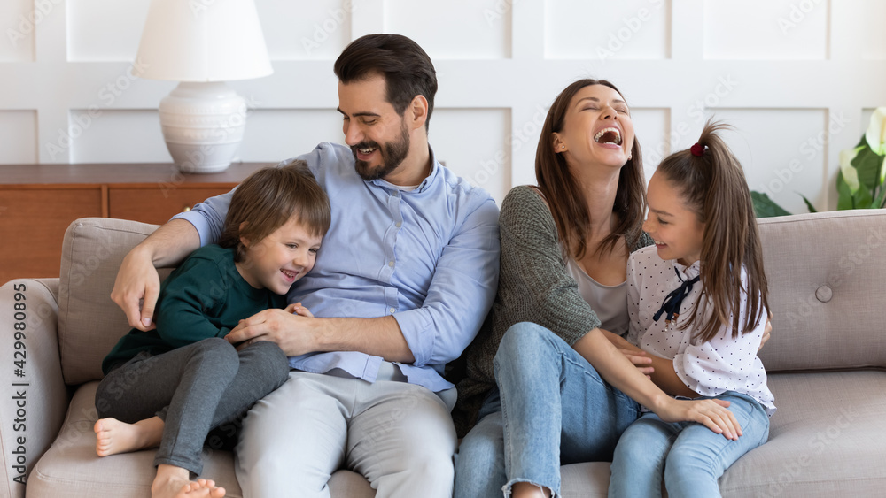 Overjoyed young Caucasian family with children have fun tickle play together in cozy modern living room. Happy parents feel playful enjoy funny game with kids relaxing together at home on weekend. Overjoyed young Caucasian family with children have fun tickle play together in cozy modern living room. Happy parents feel playful enjoy funny game with kids relaxing together at home on weekend.