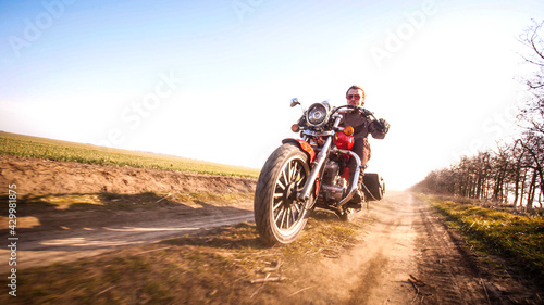 Guy in leather jacket riding through the fields off-road countryside on chopper in autumn sunny day, © Nik Viatkin
