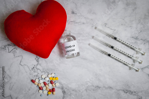 Corona Virus vaccine, syringe, pills, and red heard on the table