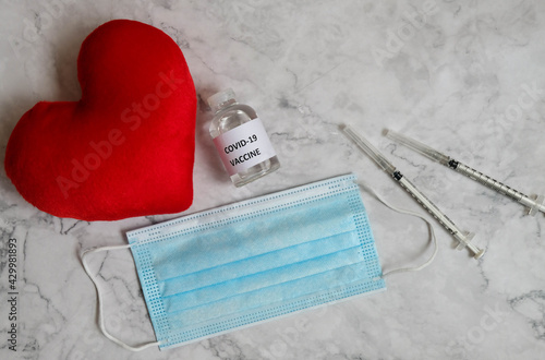 Corona Virus vaccine , mask, syringe and red heart on the table.