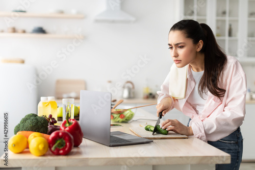 Woman cooking salad and using laptop and kitchen