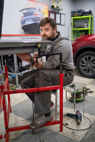 Close shot of dent removing without paint, bearded professional worker makes accurate blow rubber hammer 