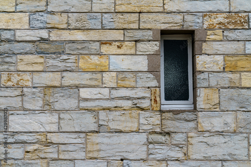 Fototapeta premium A fragment of a gray stone wall with window made of hewn stone of a rectangular shape.