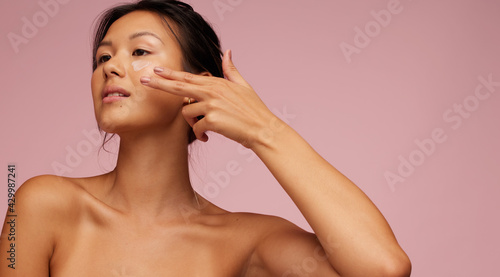Asian woman applying anti-aging cream on her face