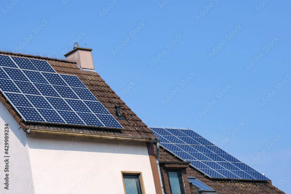 The tiled roof of the house with a chimney is covered with solar panels. Blue sky.