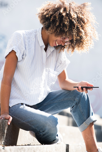 smiling young black woman sitting outside looking at mobile phone © mimagephotos