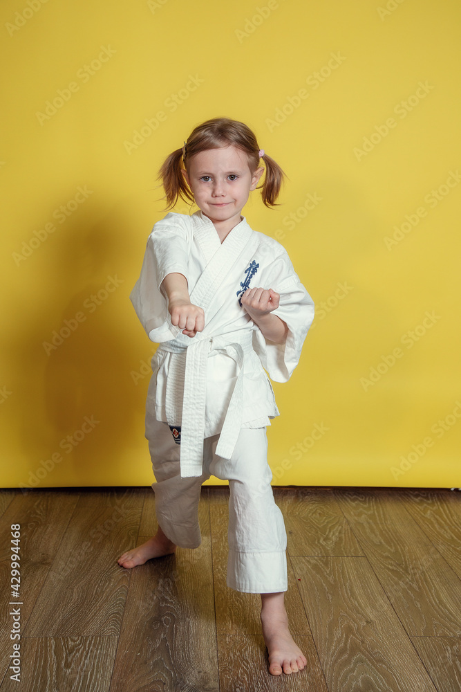 Portrait Of little caucasian Girl Practicing Karate Against yellow Background