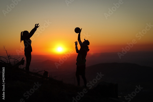 Young volleyball couple enjoying the top of a pink mountain with a ball at sunset. Silhouettes of a woman and a player pinching their fingers with a ball. Volleyball spiking, bump. Overhead passing