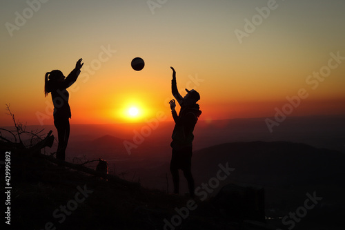 Young volleyball couple enjoying the top of a pink mountain with a ball at sunset. Silhouettes of a woman and a player pinching their fingers with a ball. Volleyball spiking, bump. Overhead passing