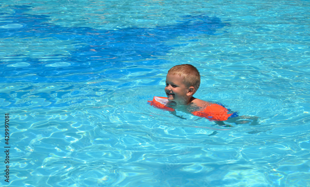 The boy bathes in the pool. Learns to swim independently with the help of inflatable armbands.