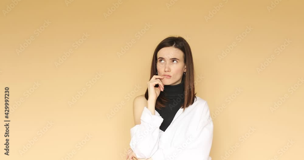 Pensive puzzled young girl wearing white shirt posing isolated on beige color background in studio. People lifestyle concept. Looking aside up put hand prop up on chin. Pensive puzzled young girl wearing white shirt posing isolated on beige color background in studio. People lifestyle concept. Looking aside up put hand prop up on chin.