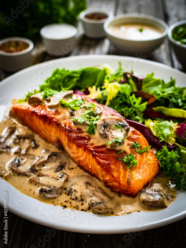 Fried salmon steak in mushroom sauce and vegetable salad served on wooden table 