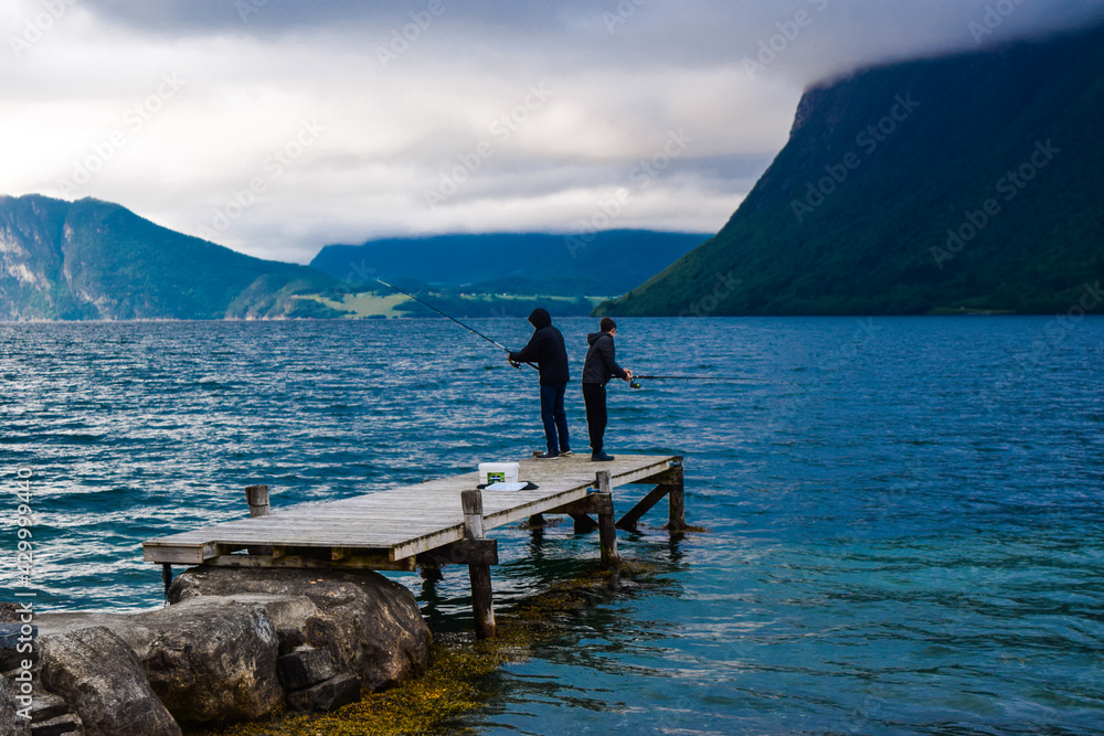 Guy and man are fishing with fishing rods in Romsdal Fjord (Romsdalsfjord). Andalsnes. Norway.