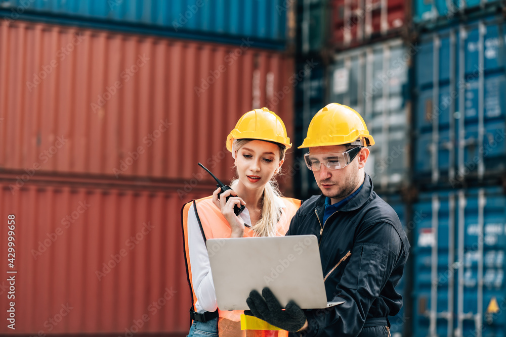 workers teamwork man and woman in safety jumpsuit with yellow helmet using laptop and talking at cargo container.female and male work in dock warehouse. transport import,export logistic industrial workers teamwork man and woman in safety jumpsuit with yellow helmet using laptop and talking at cargo container.female and male work in dock warehouse. transport import,export logistic industrial