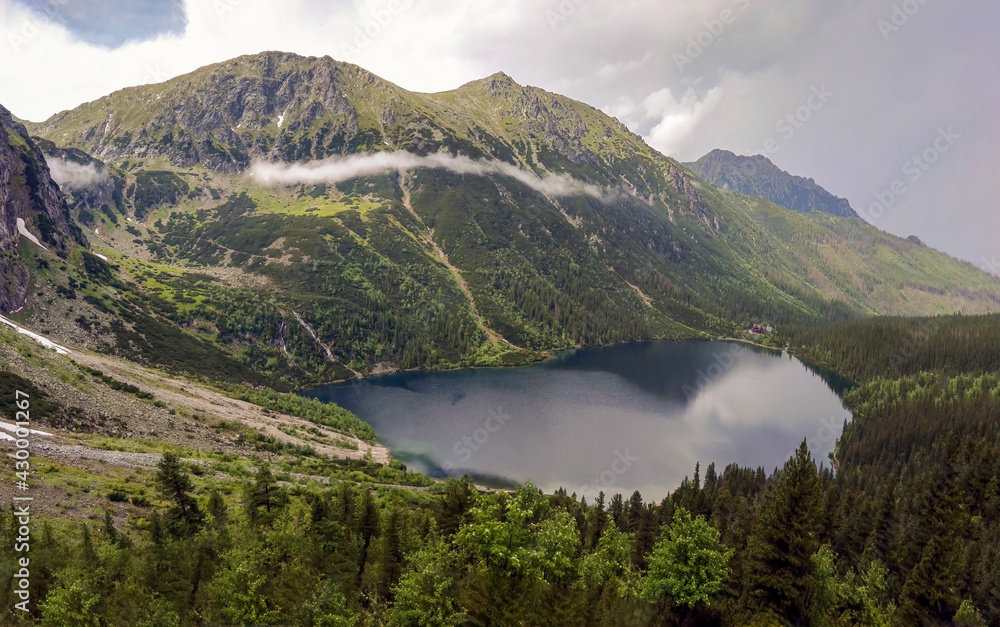 Wide angle top view of Morskie Oko naturally formed lake pond in Tatra Mountains in Poland. High mountain landscape with dramatic clouds covered with snow and trees at national park High Tatras Europe