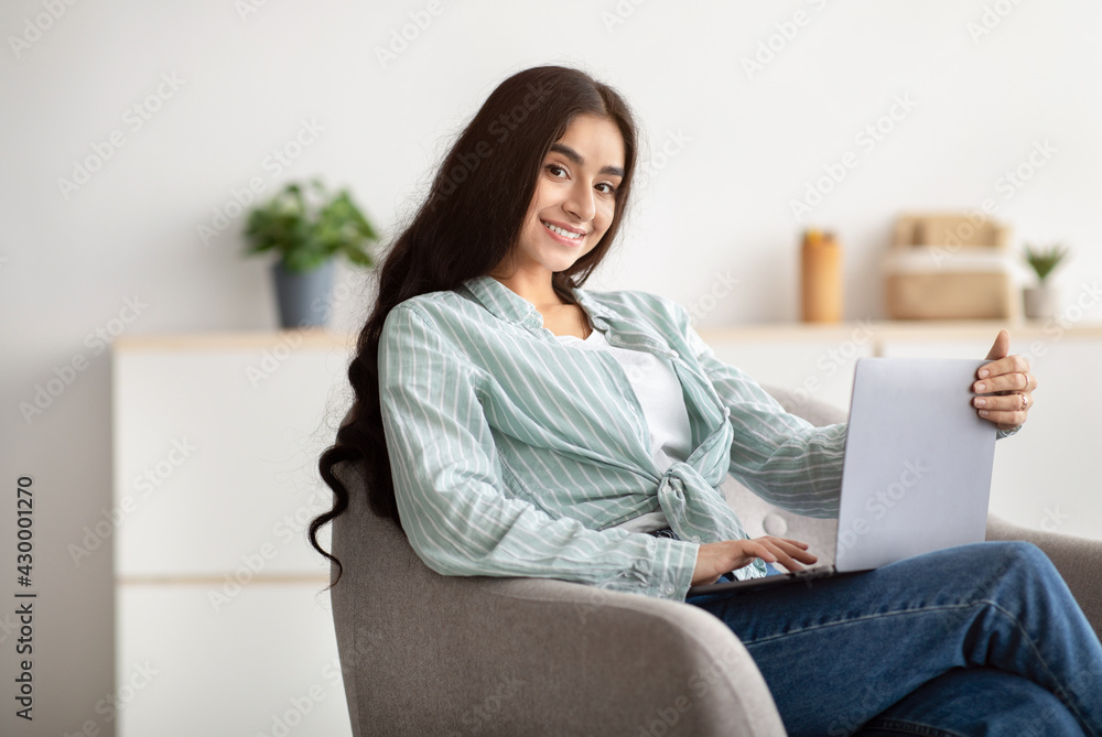 Happy Indian lady sitting in armchair with modern laptop, studying remotely or having business meeting at home Happy Indian lady sitting in armchair with modern laptop, studying remotely or having business meeting at home