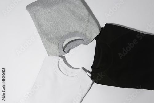 Three perfectly folded monochrome sweatshirts gray, black and white laid out in a circle isolated over white background