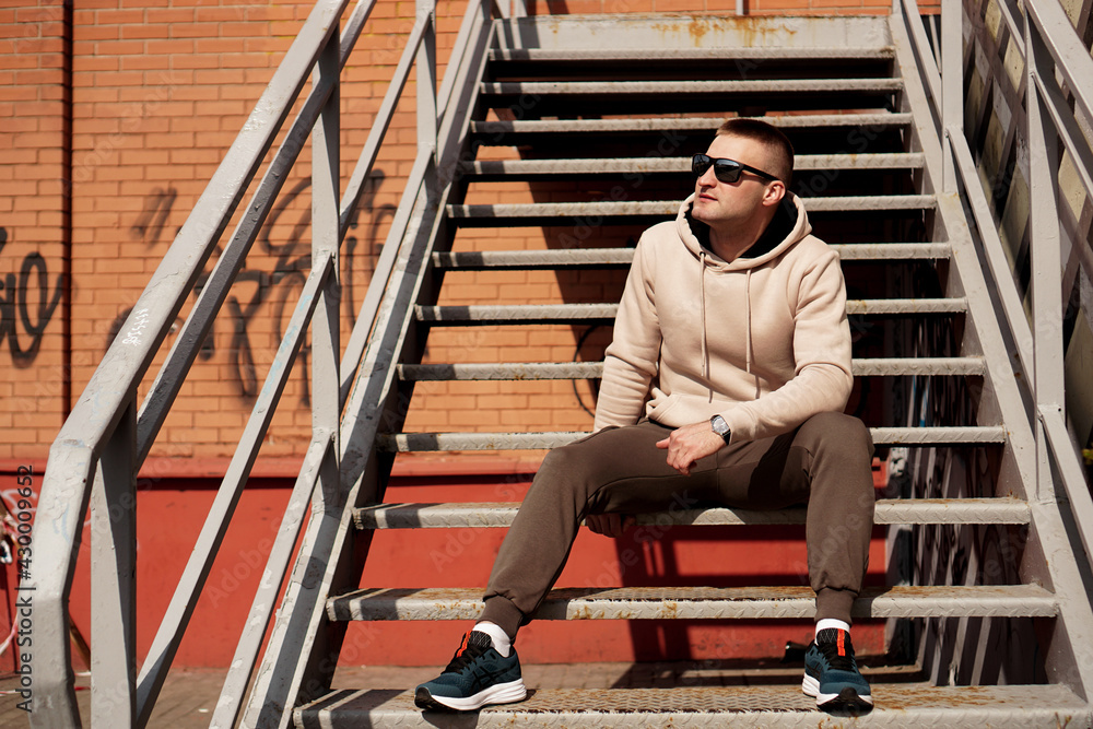 A young man sits on the steps in the city. Urban style. Lifestyle photo