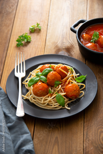 Meatballs with tomato sauce and spaghetti, pasta in black mate plate on wooden background, delicious mediteranean food