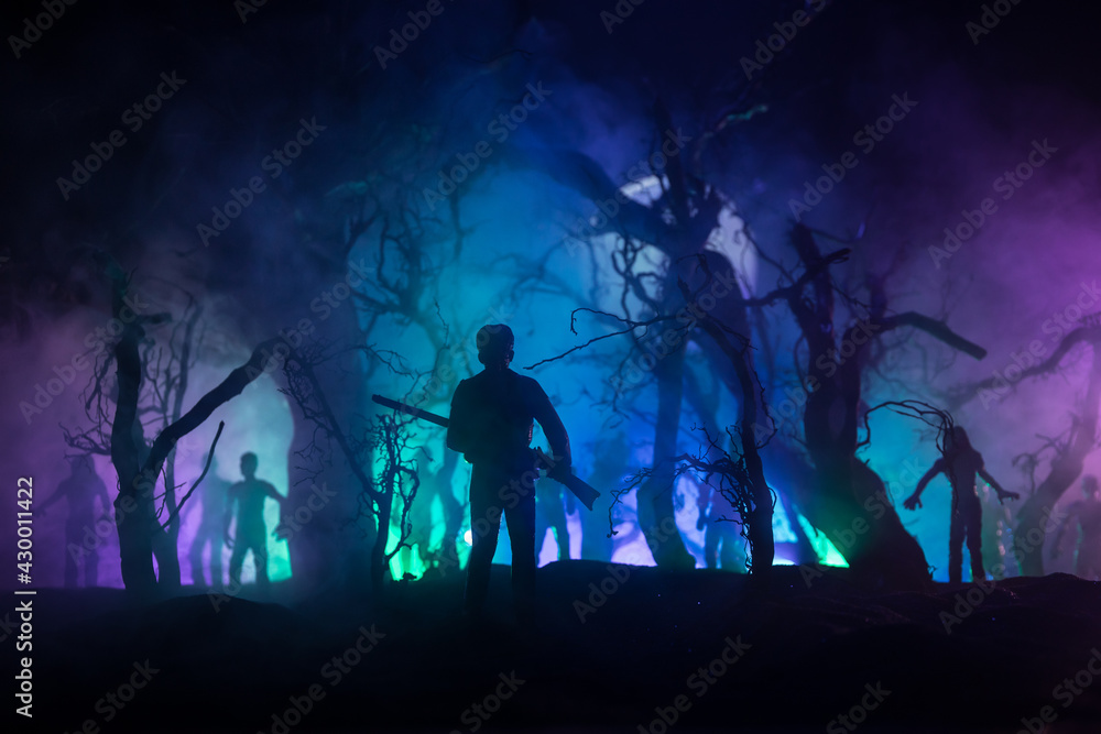 Man with riffle against zombie attack. Zombie apocalypse. Scary view of blurred zombies at cemetery and spooky cloudy sky with fog. Horror Halloween concept.