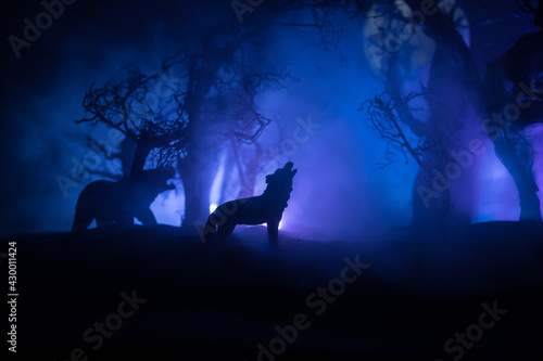 Silhouette of howling wolf against dead forest skyline and full moon. Creative artwork decoration. © zef art