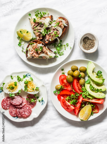 Snack, appetizers, tapas, breakfast table - salami, mackerel cream cheese sandwiches, olives, avocado, tomatoes, micro greens on a light background, top view