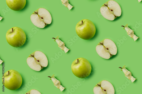 Pattern made with fresh green eaten apples and halves on the green background. Minimal organic fruit concept. Flat lay, top view.