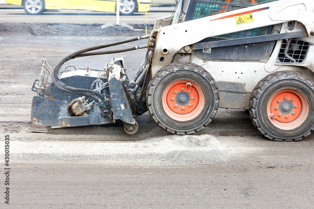 A bobcat with a surface repair attachment on asphalt plows the old surface on an asphalt road. A bobcat with a surface repair attachment on asphalt plows the old surface on an asphalt road.