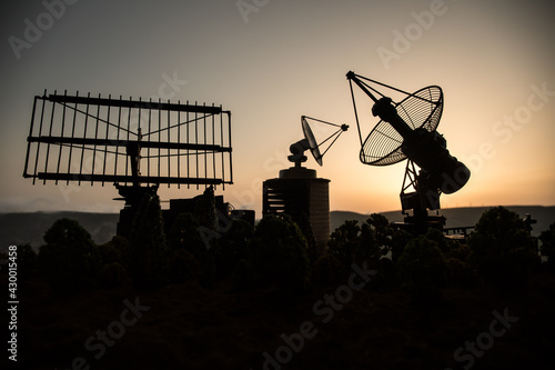Space radar antenna on sunset. Silhouettes of satellite dishes or radio antennas against night sky. Space observatory or Air defence radar over dramatic sunset sky.