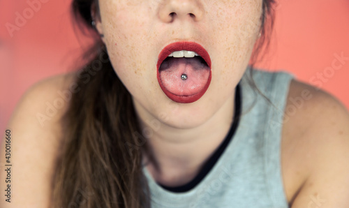 Fotografie Close up portrait of young woman with freckles sticking out pierced tongue, show
