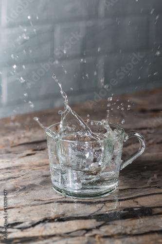 A splash of water in glass mug on the kitchen table. Clean and transparent. Lots of splashes