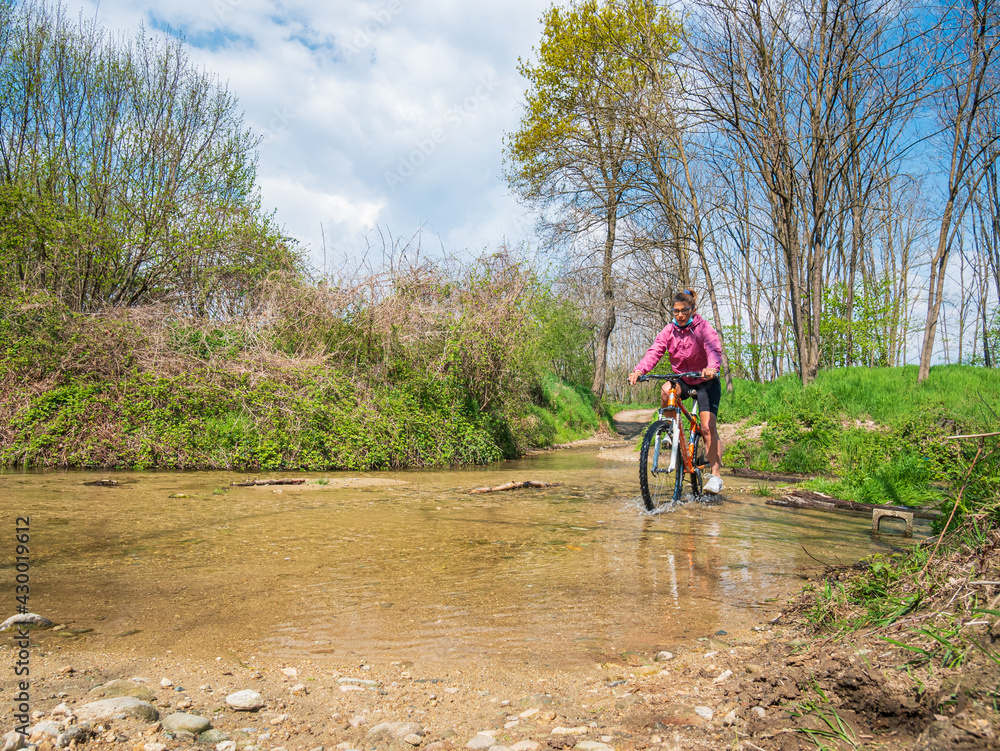 Woman having fun by riding mountain bike crosing river in a green woodland, countryside landscape, fitness wellbeing sport in nature