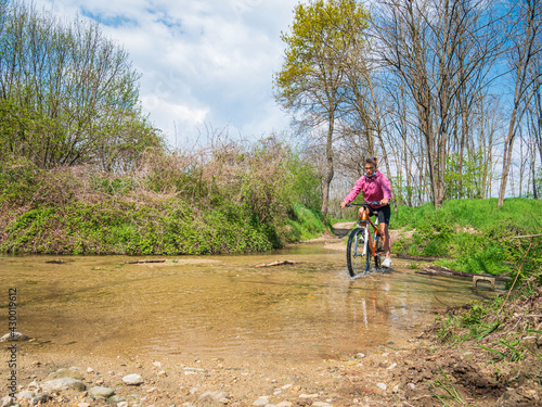 Woman having fun by riding mountain bike crosing river in a green woodland, countryside landscape, fitness wellbeing sport in nature