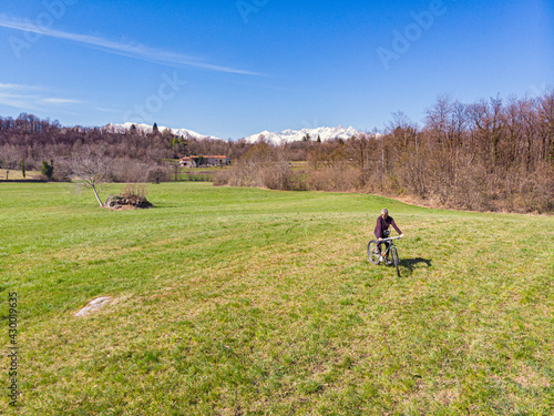 Aerial: man having fun by riding mountain bike in the grass on sunny day, scenic alpine landscape, fitness wellbeing sport in nature