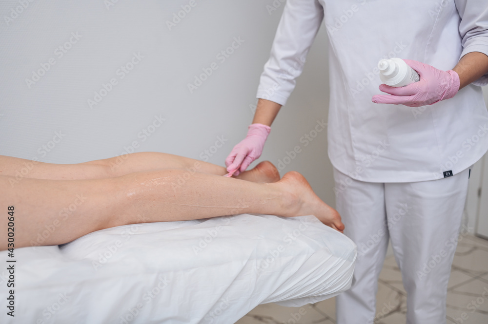 Laser epilation and cosmetology in beauty salon, spa concept. Preparation for the procedure of laser hair removal. Application of gel, disposable spatula. Beautiful smooth female legs Laser epilation and cosmetology in beauty salon, spa concept. Preparation for the procedure of laser hair removal. Application of gel, disposable spatula. Beautiful smooth female legs