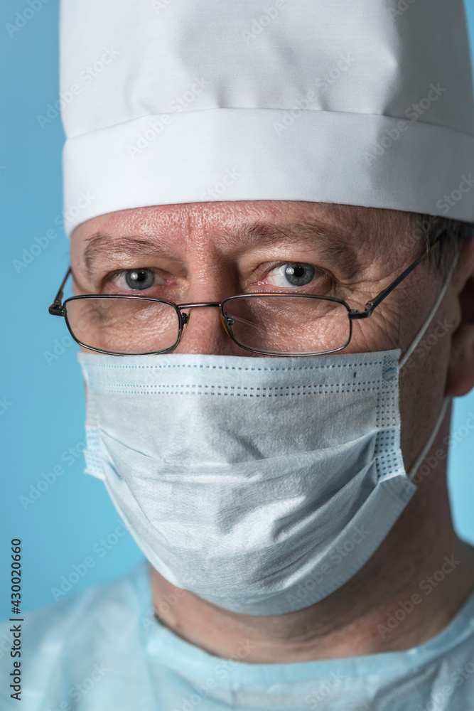 Portrait of middle-aged experienced doctor in a medical cap and mask, wearing glasses. Close-up view of the camera Portrait of middle-aged experienced doctor in a medical cap and mask, wearing glasses. Close-up view of the camera
