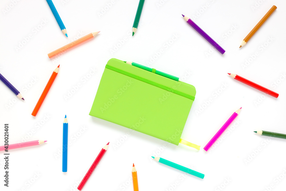 closed green notepad on white background near pencils