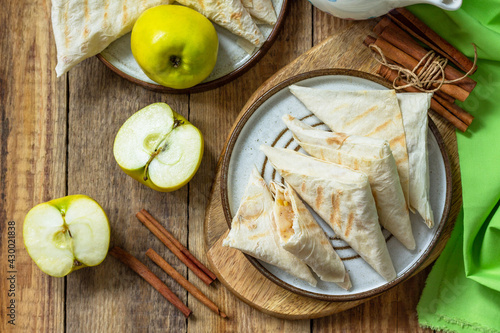 Apple pastries for breakfast. Grilled lavash triangle with apples and cinnamon on a wooden wooden table. Top view, flat lay.