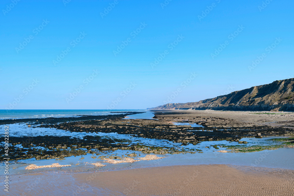La plage et les falaises du port en Bessin en France, en Normandie, dans le Calvados, au bord de la Manche sous le Soleil.