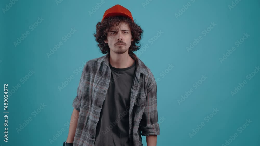 The charismatic young man, energetically puts his cap on his head, looks questioningly forward and then angrily jumps up and breathes his sleeve. isolated over turquoise background.Concept of life The charismatic young man, energetically puts his cap on his head, looks questioningly forward and then angrily jumps up and breathes his sleeve. isolated over turquoise background.Concept of life